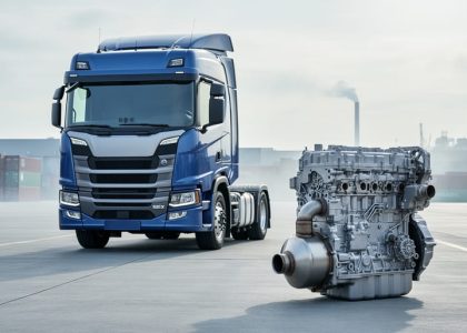 “Heavy-duty diesel truck and emission-control components on a maintenance apron with a distant industrial yard background.”